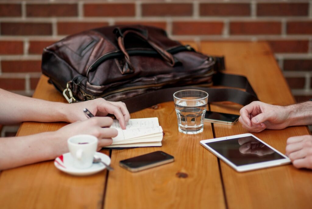 Two people reviewing notes, a tablet and phone across a wooden table